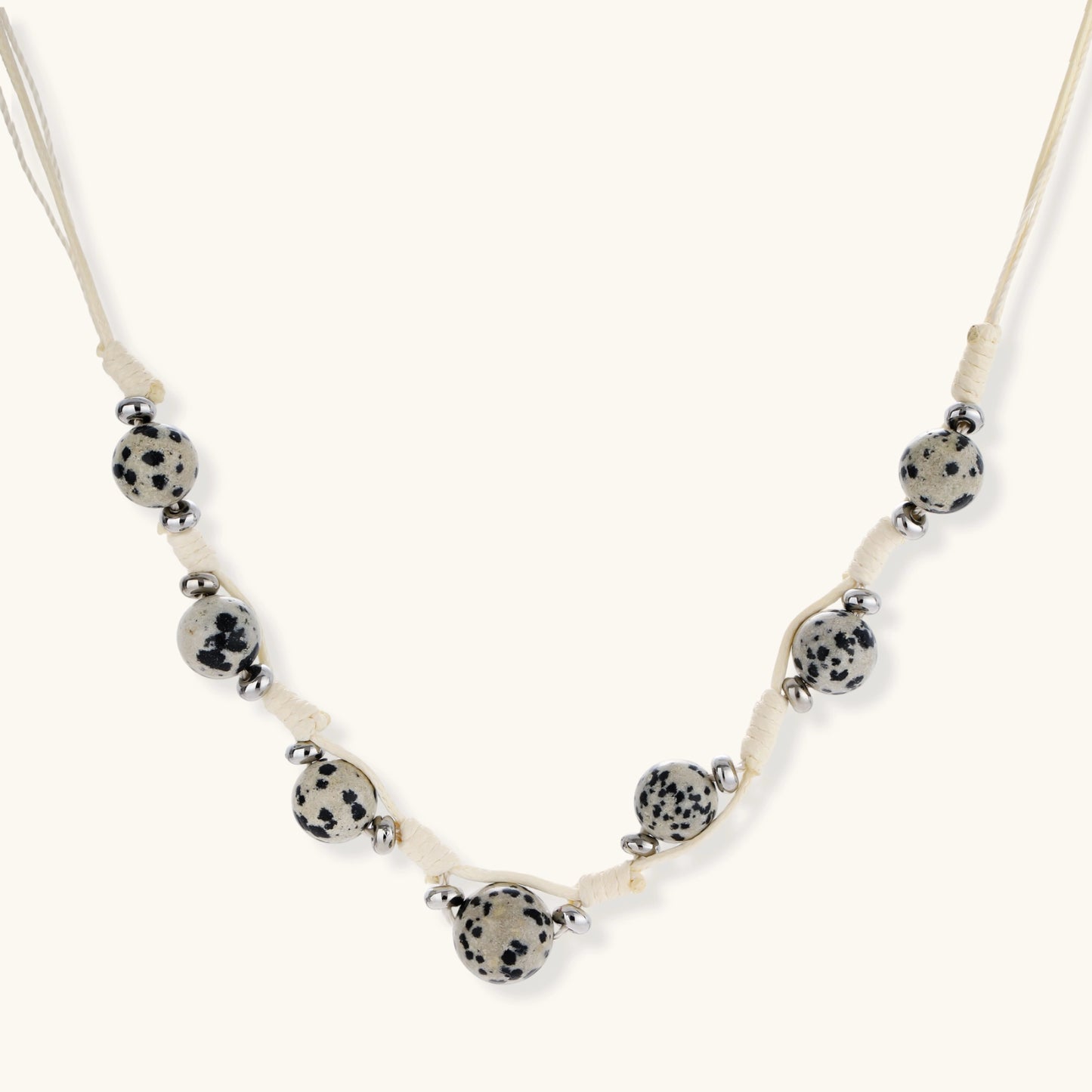 Adjustable cream cord necklace with white spotted stone beads featuring black speckles on neutral background